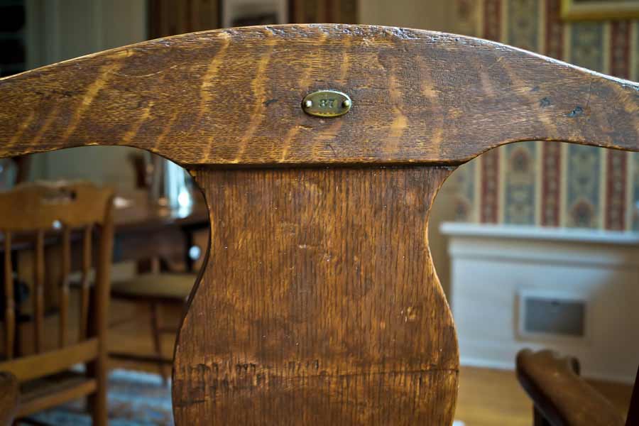 close up photo showing Brass ID plate on back of 1087 Armchair, purchased by Cass Gilbert for the 1905 Minnesota State Capitol, carved wood with fabric cushion seat cover